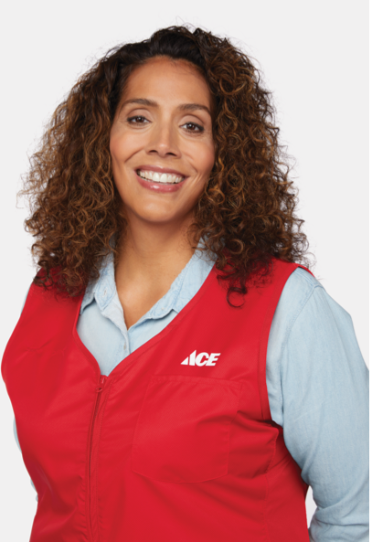 A woman with curly hair smiles at the camera, wearing a red vest with an "ACE" logo over a light blue shirt.